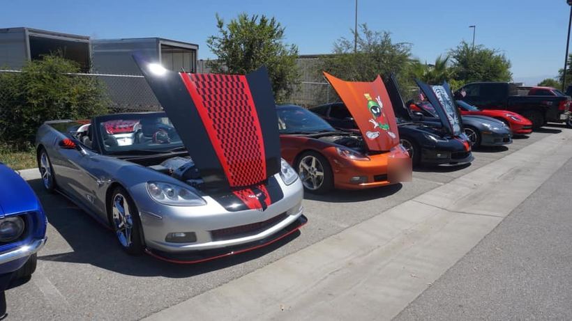 A row of Corvettes at an outdoor car show, hoods up