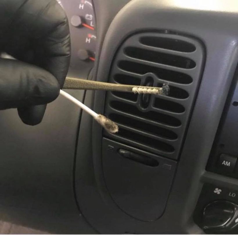 Gloved hand cleaning a dash vent with a swab during an interior detail